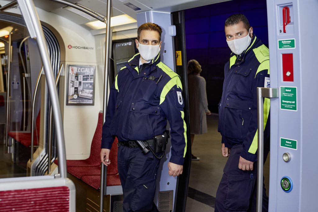 Zwei Mitarbeiter der Hochbahn/Prüfer betreten eine U-Bahn. Sie tragen medizinische Masken.