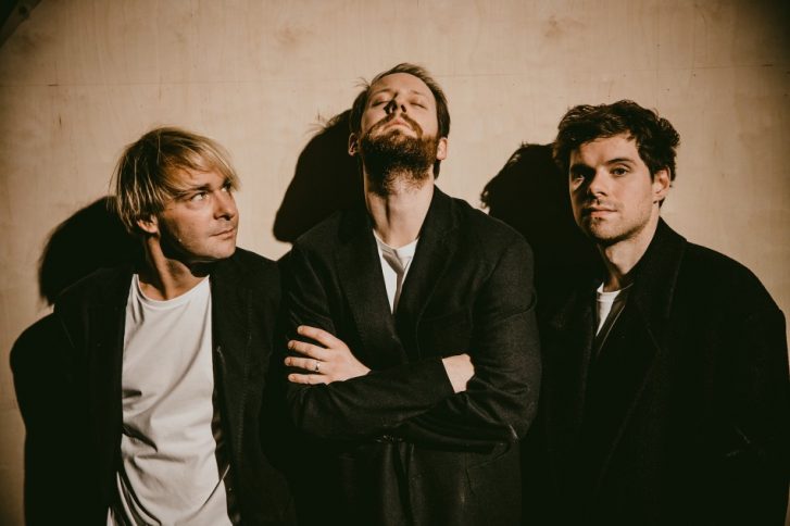 Drei Schauspieler vor einer Wand. Es ist dunkel.