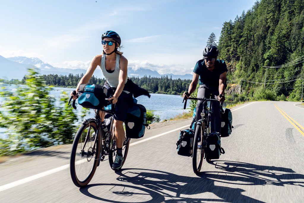 Radreisen – Eine Radfahrerin und ein Radfahrer auf einer Tour entlang eines Sees