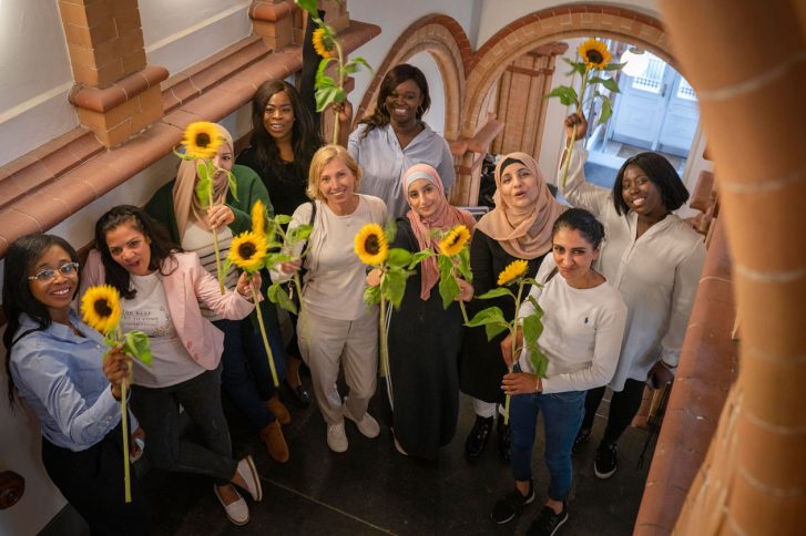 Das Fot zeigt Stadtteilmütter in einem schönen Treppenhaus. Sie halten Sonnenblumen in die Kamera. - Stadtteilmütter : Ruth, Sükran, Fatima, Rudaina, Rita, Rahael, Meltem, Heba, Evon und Shawna (v.r.) // Foto: © shutterstock | Rido